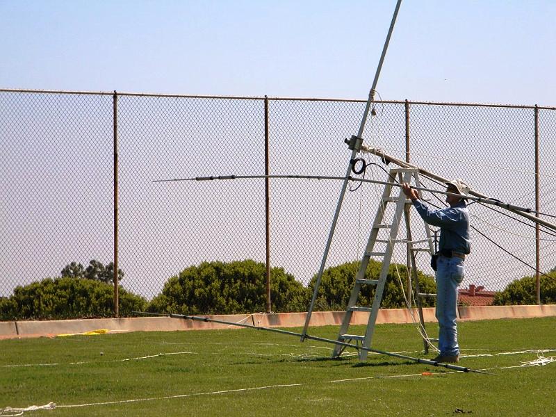 020.JPG - Man with beam antenna down, against the chain link fence:  Bob Closson, W6HIP, took down SSB antenna for additional tuning adjustments on traps just before start of Field Day.